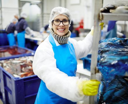 Smiling staff of seafood processing plant pushing huge cart with packed fish